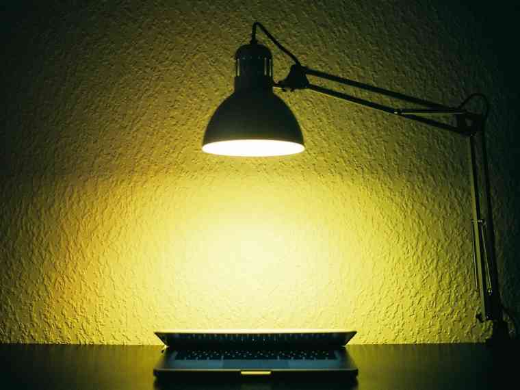 Eine kleine Lampe ist die einzige Beleutung an einem Schreibtisch.
