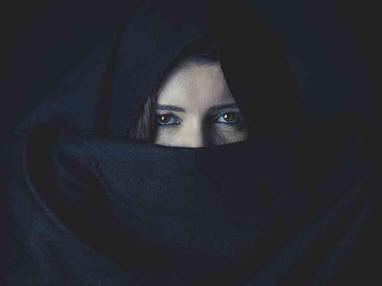 Der Blick einer Frau, deren Gesicht mit einem schwarzen Tuch verhüllt ist.