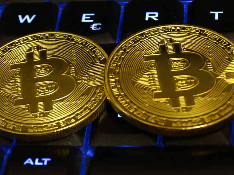 Das Bild zeigt zwei Bitcoins auf einer beleuchteten Computer-Tastatur. 