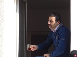 Ein ausländischer Mann mit einem Schnurrbart sitzt an einem offenen Fenster, schaut nach links und hält eine Teetasse in der Hand.