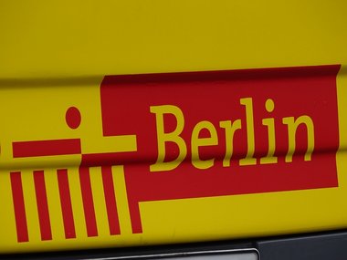 Ein Berliner Schriftzug in gelb auf rot gelben Hintergrund mit symbolischer Darstellung des Brandenburger Tores.