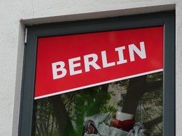 Ein Fenster in dem am oberen Rand ein schräger Aufkleber mit dem Wort Berlin in weißer Schrift auf rotem Grund klebt.