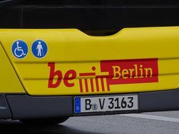 Der moderne Berlinschriftzug in rot gelb auf einem Bus mit einem Berlin-Kennzeichen und zwei Zeichen für Gehbehinderte und Rollstuhlfahrer.