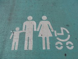 Eine mit Männchen dargestellte Familie in weiß auf türkisfarbenem Boden mit Sohn, Vater, Mutter und Kinderwagen.