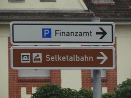 Ein weißes Schild mit Pfeil nach rechts und der Aufschrift -Finanzamt- und ein Parkplatzsymbol sowie ein braunes Schils mit dem Hinweis für P+R für die Selketalbahn.