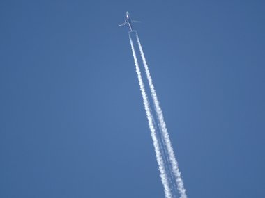 Ein Flugzeug mit langem, weißen Kondensstreifen am blauen Himmel.