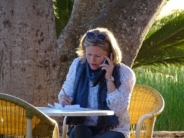 Eine telefonierende Frau sitzt an einem Tisch mit Zettel und Stift.