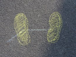 Ein mit gelber Kreide auf den Straßenbelag aufgemalter Fußabdruck von zwei Füßen in Schrittstellung.
