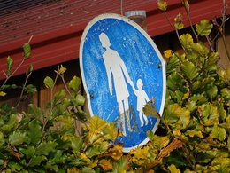 Ein veraltetes Fußgängerschild mit einer Frau und einem Kind in einer Hecke.
