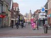 Eine Fußgängerzone in Holland mit Geschäften und Passanten, teilweise auf Fahrrädern unterwegs.