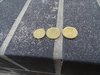 Drei Geldmünzen liegen nebeneinander auf einem sandigen Boden.