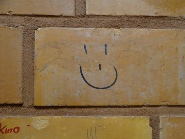 Rote Ziegelsteinmauer in einer Turnhallenkabine auf dem ein lachendes Gesicht aufgemalt ist.