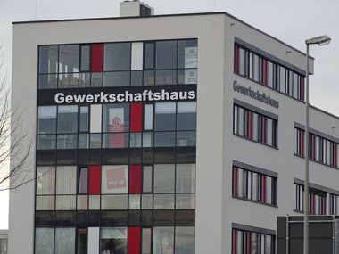 Ein hohes, großes  Gebäude in Grau- und Rottönen und der weißen Aufschrift Gewerkschaftshaus.