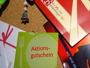 Eine Pinnwand mit Gutscheinen z.B. einen grünen Aktionsgutschein und einen von einem Restaurant mit Namen Brandenburger Tor.