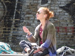 Eine junge Frau mit Sonnenbrille und Ohrstöpsel hält ein Kaffee und eine Zigarette in der Hand. 