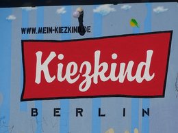 Das rote Schild Kiezkind auf einer blauen Wand in Berlin aufgemalt.