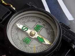 Ein schwarzer Kompass mit einem weißen Zifferblatt und grünen Richtungsanzeigern.