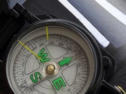 Ein schwarzer Kompass mit einem weißen Zifferblatt und grünen Richtungsanzeigern.