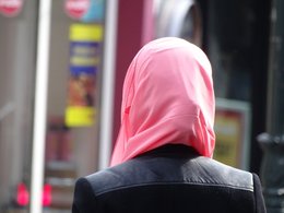 Eine Frau von hinten mit schwarzer Jacke und rotem Kopftuch.