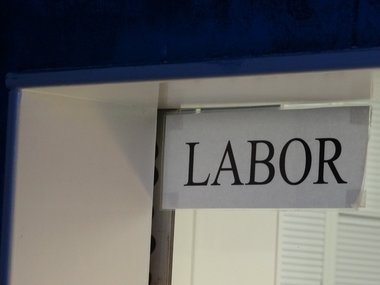 Ein weißes Schild mit schwarzer Aufschrift: Labor sowie ein angedeuteter Raum im Hintergrund.