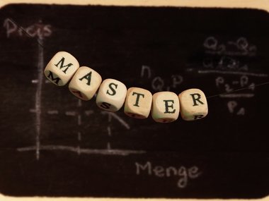 Buchstabenwürfel an einem Faden ergeben das Wort Master und mit einer Tafel mit einer Diagrammkurve im Hintergrund.