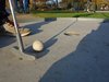 Das ende eines minigolfschlägers mit einem ball davor auf der bahn kurz vr dem zutreffendem loch