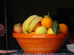 Ein Obstschale in orange gefüllt mit Bananen, Äpfen, Orangen und Zitronen in einem offenen Fenster.