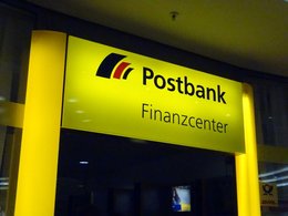 Ein gelb leuchtender Eingang von einem Finanzcenter der Postbank.