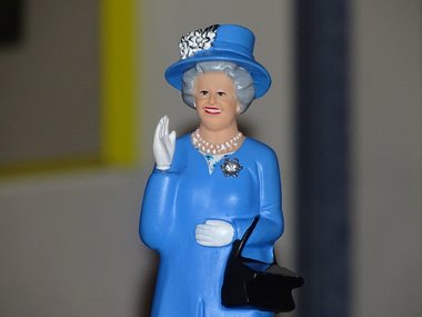 Foto einer Figur der englischen Königin Queen Mum in einem blaune Kleid. Sie hat stilvoll die rechte Hand zum Gruß gehoben.