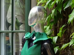 Ein Schaufensterpuppenkopf in silber ohne Haare mit einem grünen Oberteil.