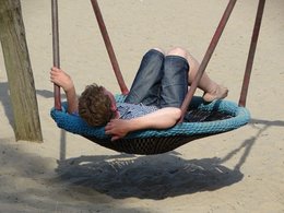 Ein junger Mann liegt in einer Hängeschaukel ohne Schuhe und darunter ist Sand.