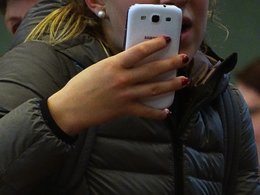 Junges Mädchen in Daunenjacke, die auf ihr weißes Smartphone schaut.