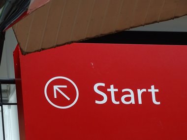 Rotes Hinweisschild in einem Museum zum Start mit einem eingekreistem Pfeil.