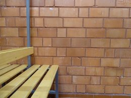 Holzbank in einer leeren Turnhallenkabine mit roter Ziegelsteinmauer.