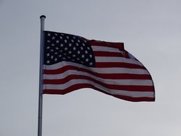 An einem Fahnenmast wehende Flagge der USA vor blaugrauem Himmel.