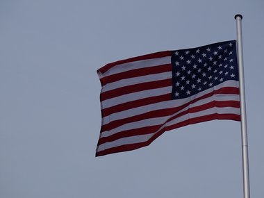 An einem Fahnenmast wehende Flagge der USA vor blaugrauem Himmel.