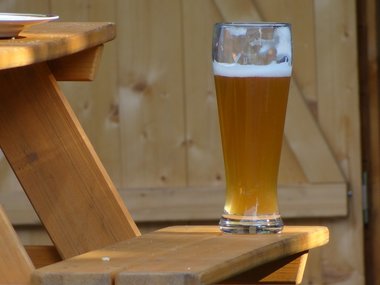 Ein Glas Weizenbier steht auf einer Holzbank.