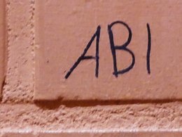 Rote Ziegelsteinmauer in einer Turnhallenkabine auf dem das Wort ABI geschrieben steht.