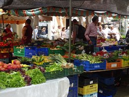 Eine Marktszene mit Obst, Gemüse und Einkäufern.