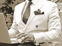 Ein Mann im weißen Anzug mit gepunkteter Krawatte arbeitet an einem Notebook.