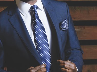 Der Oberkörper eines Mannes mit blauem Anzug und gepunkteter Krawatte.