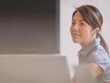 Eine Asiatin sitzt lächelnd am Computer.
