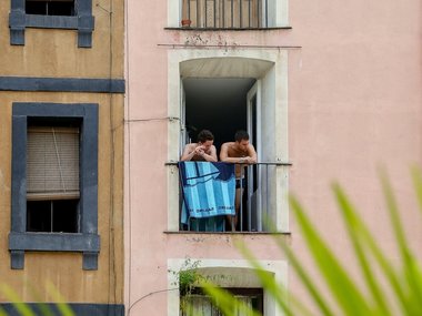 Zwei junge Männer stehen an einem offenen Fenster am Geländer mit Handtuch und schauen zur Seite.