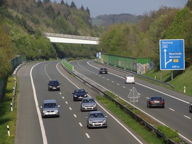 Eine leicht, mit Autos befahreren Autobahn mit einem Verkehrsschild und einer Brücke im Hintergrund.