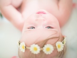 Ein Baby mit einem Blumenkranz im Haar liegt auf dem Rücken.