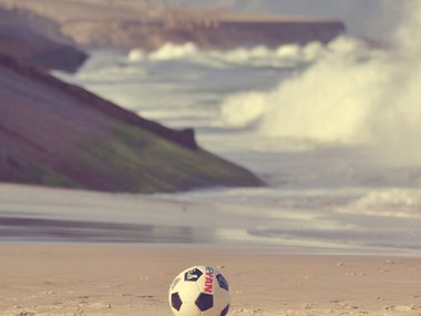 Ein Fußball liegt am Strand.