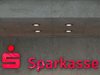 Das rote Symbol und die plastischen Buchstaben für die Sparkasse hängen an einer grauen Wand.