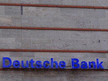 Die plastischen, blauen Buchstaben von der Deutschen Bank hängen an einer Hauswand im unteren Teil des Bildes.