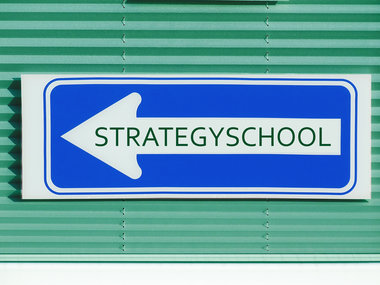 Ein blaues Schild mit der Aufschrift "Strategy School" und einem Pfeil nach links.
