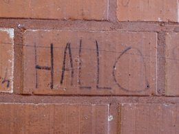 Rote Ziegelsteinmauer in einer Turnhallenkabine auf dem das Wort Hallo geschrieben steht.